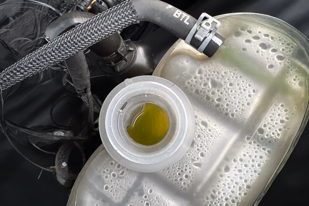 Close-up of a car coolant reservoir with yellow-green coolant fluid inside, connected to hoses.