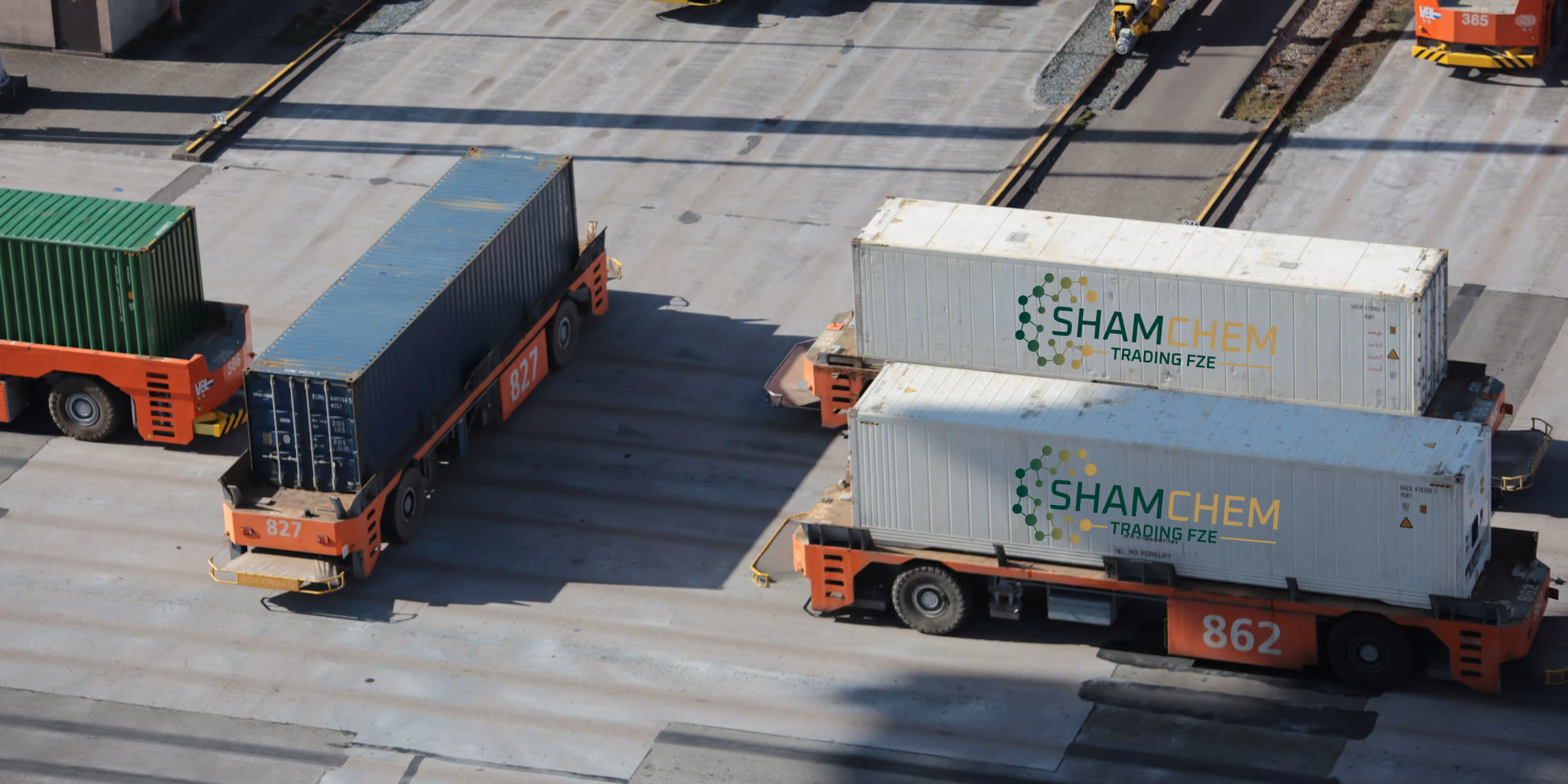 Three cargo trucks carrying shipping containers, two white with ShamChem logo, one green and blue.