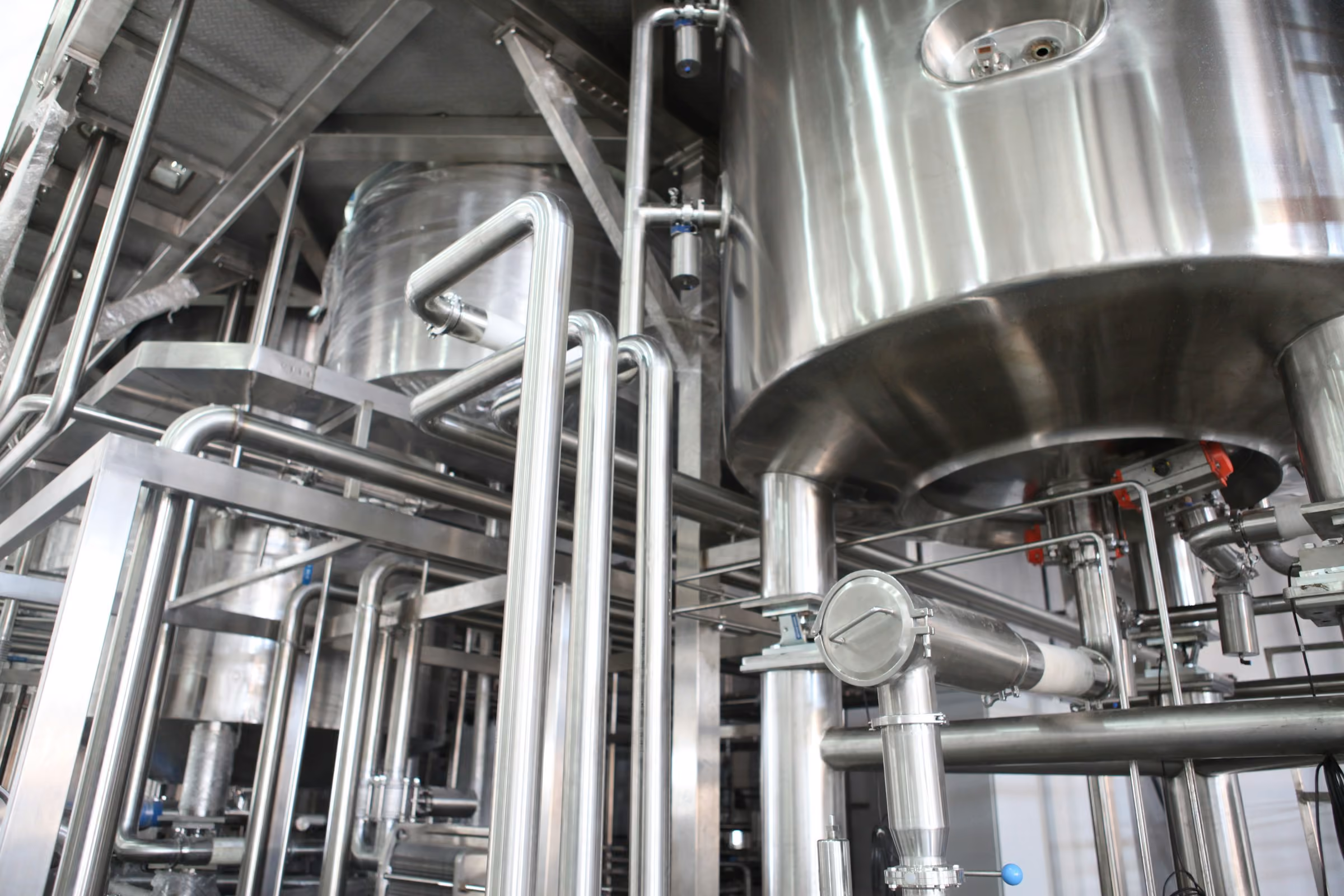 Stainless steel industrial pipes and tanks inside a processing plant.