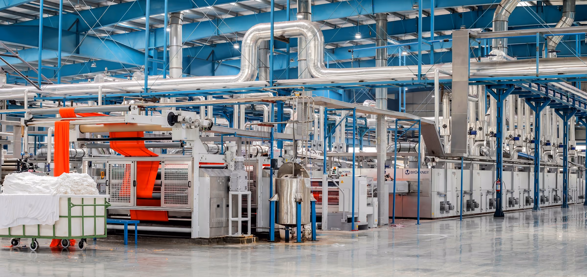 Large textile factory interior with machines producing red fabric and textile carts on shiny floor.