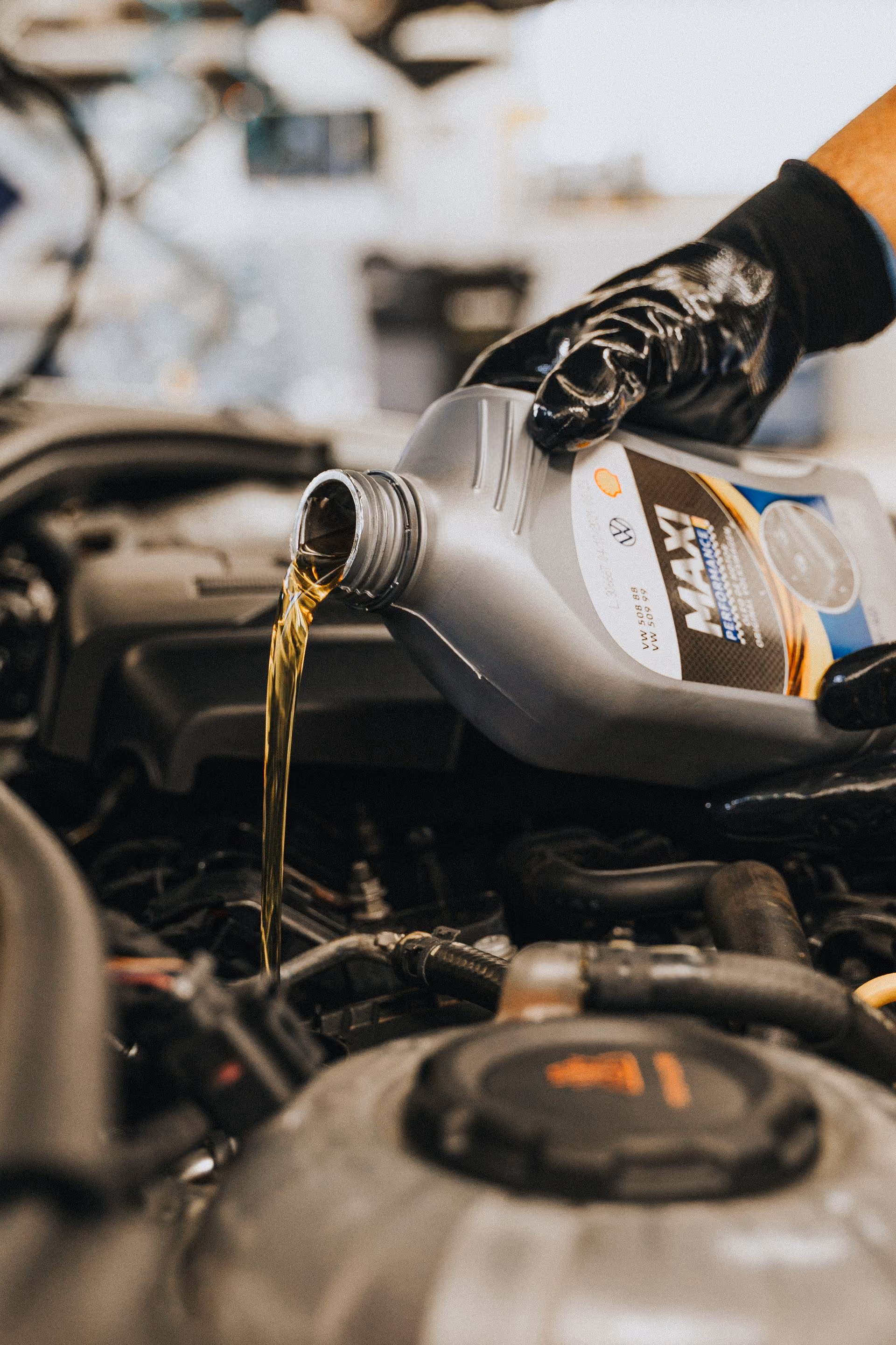 Gloved hand pouring motor oil from a container into a car engine.