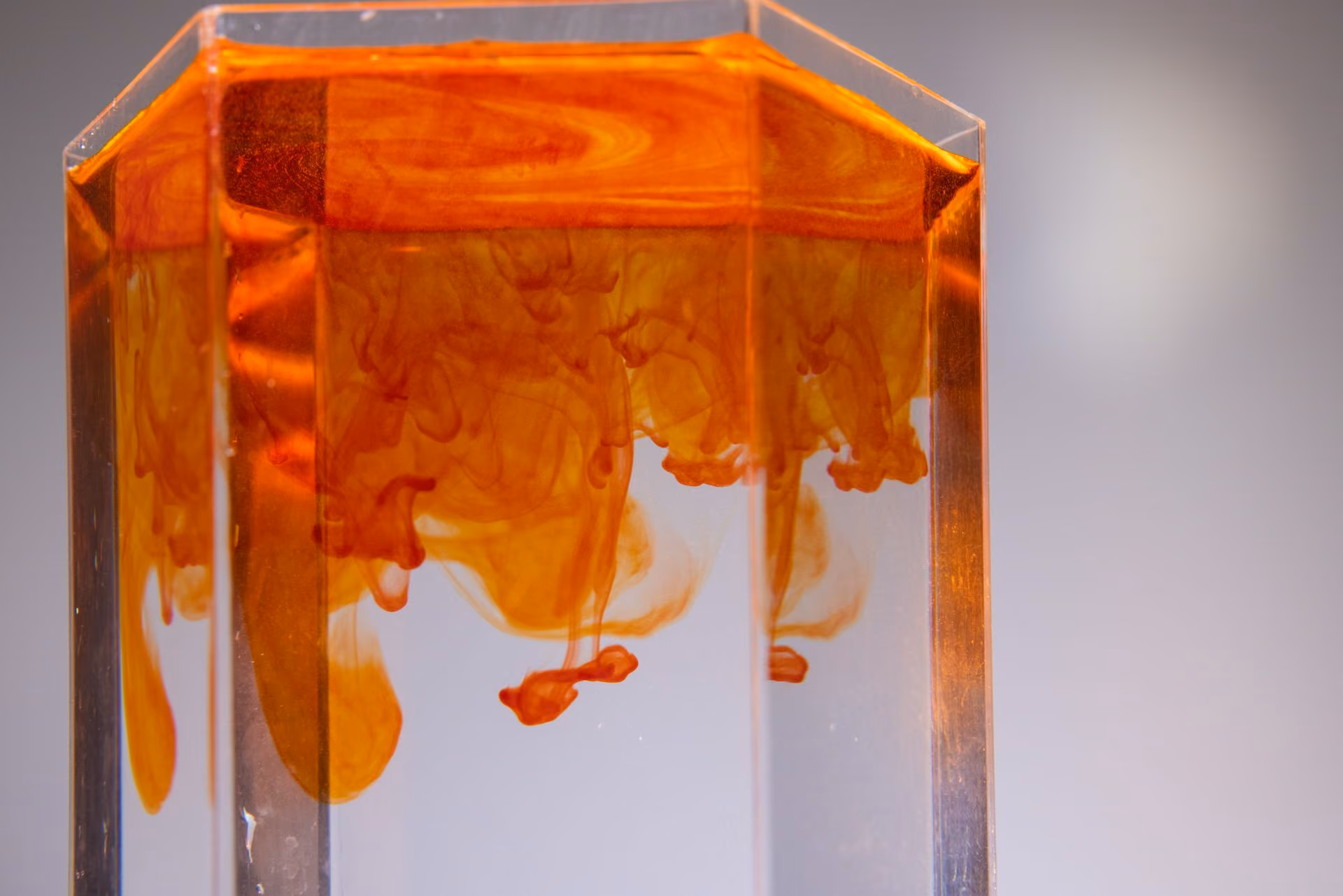 Orange liquid swirling and diffusing in a clear rectangular container filled with water.