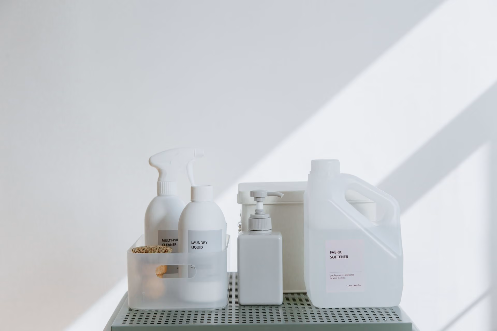 White cleaning and laundry bottles arranged on a shelf with sunlight casting shadows.