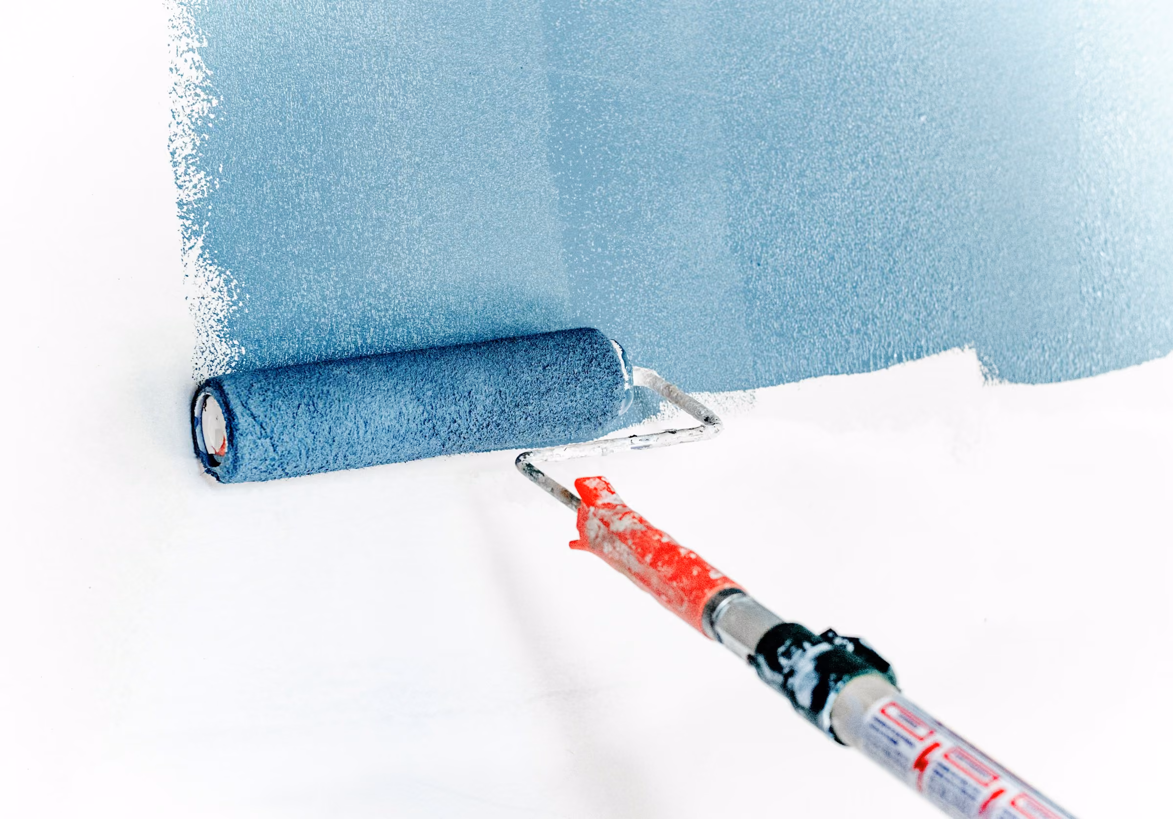 Paint roller with blue paint applying a coat on a white wall.